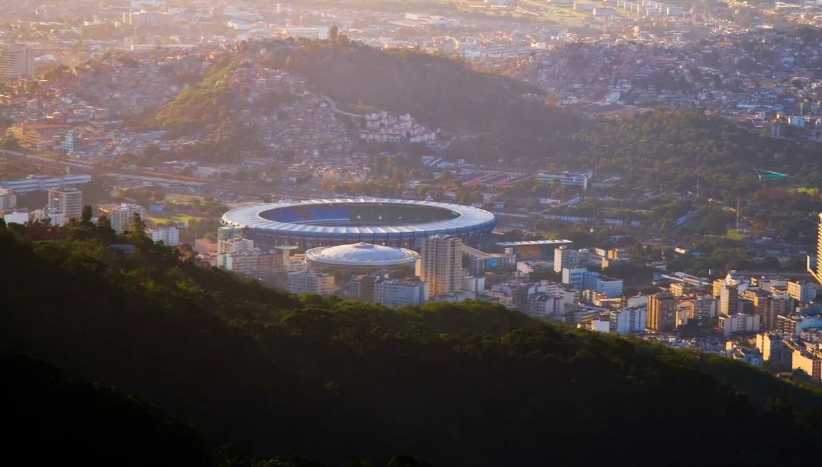 Estádio visto de longe, com a cidade e o pôr do sol ao fundo